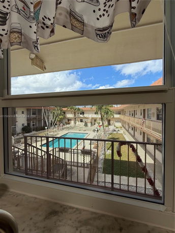 View of a swimming pool area surrounded by residential buildings, seen through a window.