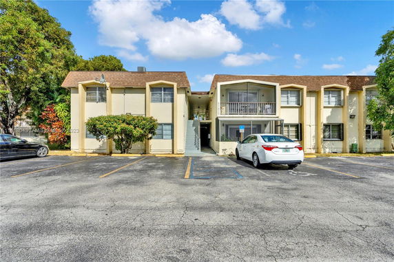 Front view of a two-story apartment building with adjacent parking spaces.