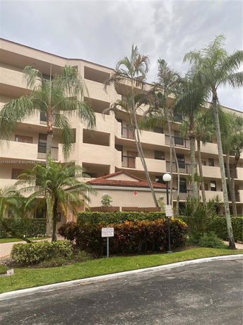 Front view of a multi-story apartment building with balconies and surrounded by palm trees.