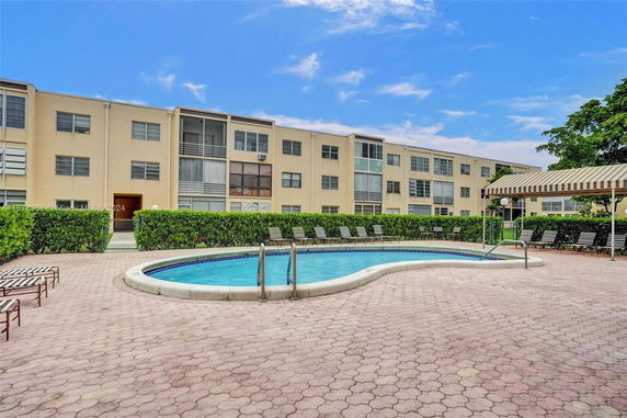 Outdoor swimming pool area in front of a multi-story residential building.