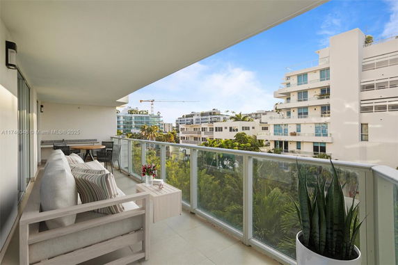 Panoramic view from a balcony overlooking modern white buildings with greenery and a clear blue sky.