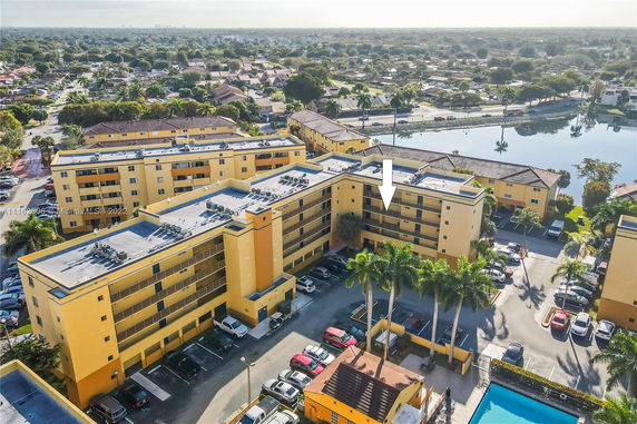 Aerial view of a multi-story yellow apartment complex with surrounding neighborhood and water body.