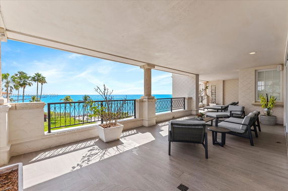 Covered outdoor seating area with ocean view and wrought iron railing.