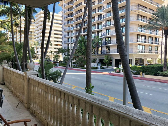 View of tall, modern residential buildings with balconies from a nearby balcony, with palm trees visible in the foreground.