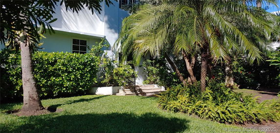 Front view of a residential building partially obscured by trees and shrubs.