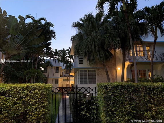 Front view of a two-story house with palm trees and a gated entrance.