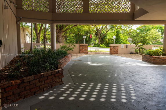 Covered outdoor parking area with brick planters and patterned wall.