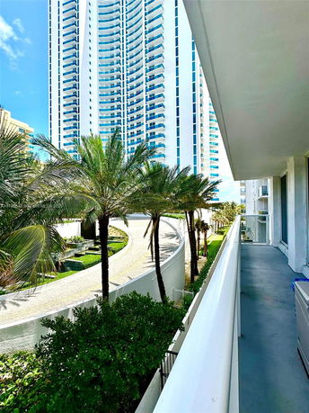 Exterior view of a high-rise building with multiple balconies and palm trees in the foreground.