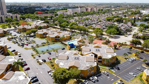 Aerial view of a residential area with multiple buildings, parking spaces, and tennis courts.