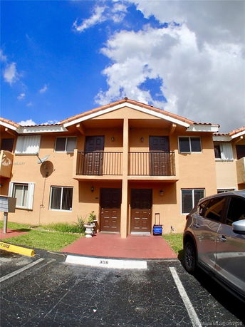 Front view of a two-story residential building with balconies and parking area.