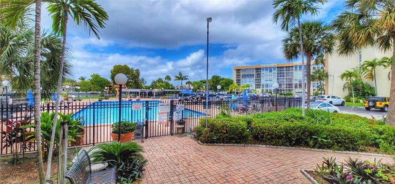 View of a multi-story building with balconies, next to a fenced swimming pool area.