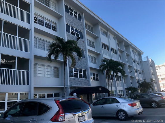 Front view of a multi-story apartment building with balconies and palm trees.