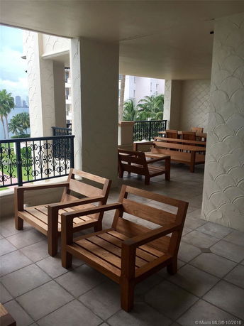 Balcony seating area with wooden chairs and tables overlooking a city skyline and palm trees.
