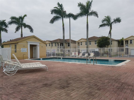 Outdoor swimming pool area with lounge chairs and palm trees.
