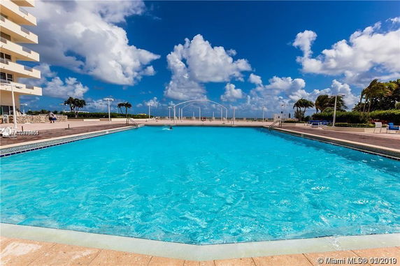 Outdoor swimming pool with tall building nearby and open sky in the background.