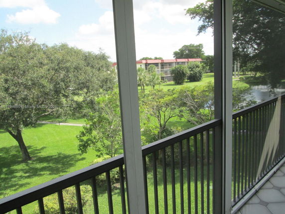 View from a balcony overlooking a green outdoor area with trees and a pond.