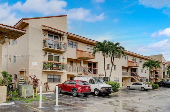 Front view of a three-story residential building with balconies and parked cars.