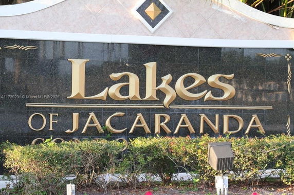 Sign with the text 'Lakes of Jacaranda' in gold letters on a dark stone background.