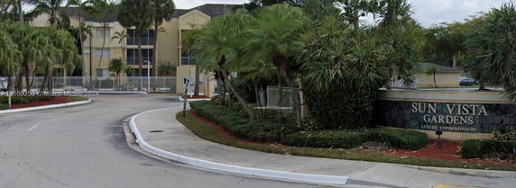 Front view of a condominium complex with an entrance sign and landscaped surroundings.