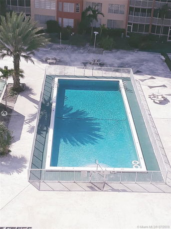 Top view of a rectangular swimming pool with surrounding fence and nearby patio area.
