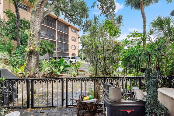 Exterior view of a multi-story building with a screened balcony and surrounding vegetation.
