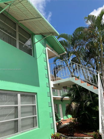 Front view of a green two-story building with exterior staircase and windows.
