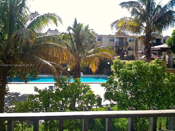 Swimming pool area surrounded by palm trees with residential buildings in the background.