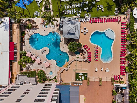 Aerial view of an outdoor area with two swimming pools surrounded by lounge chairs and palm trees.