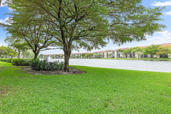 View of a lake with surrounding green grass and trees, adjacent to residential buildings.