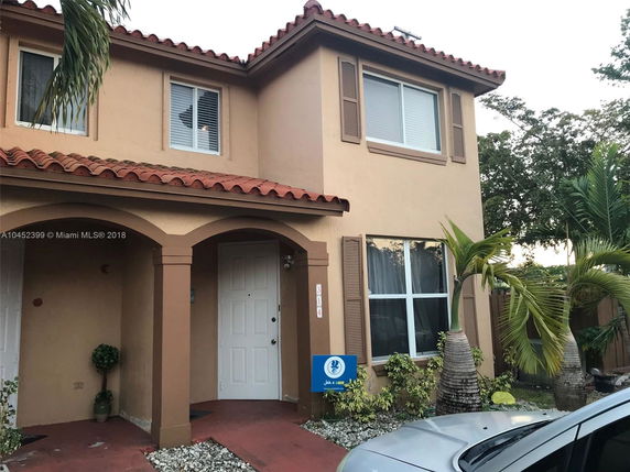 Front view of a two-story house with a red tiled roof and arched entrance.