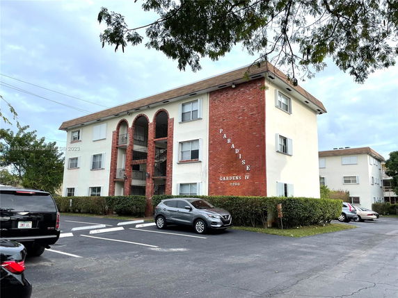 Front view of a three-story apartment building with a brick facade and parking area.