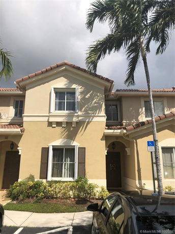 Front view of a two-story townhouse with a tile roof and arched entrance.