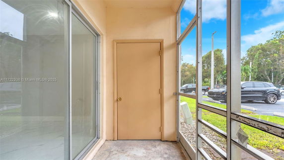 Outdoor view of a small enclosed area with a glass door and a wooden door, overlooking a parking area.