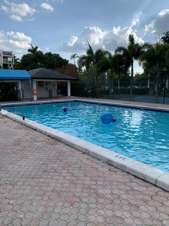 Outdoor swimming pool with a nearby building and palm trees.