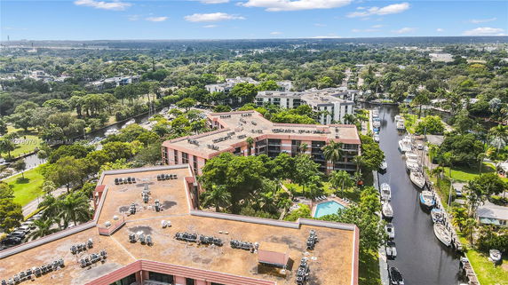 Aerial view of buildings with flat rooftops featuring numerous air conditioning units and a swimming pool surrounded by greenery.