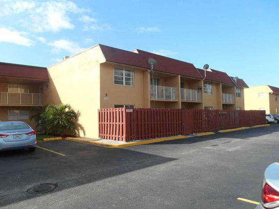 Front view of a two-story apartment building with balconies and a fenced area.