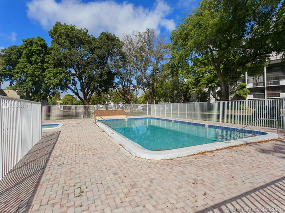 Outdoor swimming pool surrounded by a white metal fence and trees.
