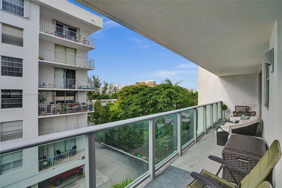 View from a balcony overlooking neighboring building with balconies and surrounding greenery.