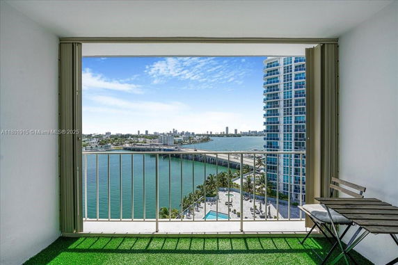 Panoramic view of a cityscape and waterbody from a balcony with artificial grass and two chairs.