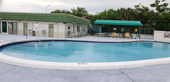 Outdoor swimming pool area with a fence and a covered seating area.