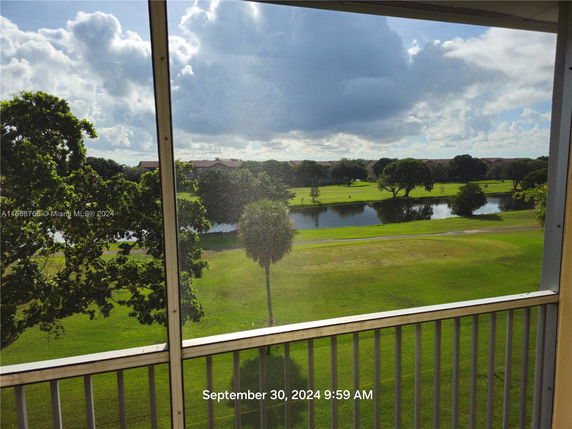 Panoramic view of a grassy area with a pond and trees, seen from a balcony.