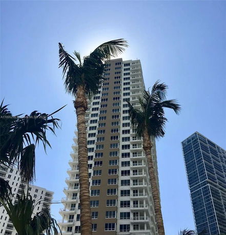Front view of a tall modern residential building with balconies and palm trees in the foreground.