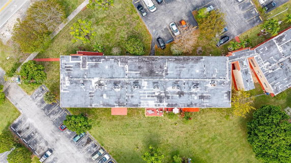 Aerial view of a building rooftop with visible parking area and greenery.