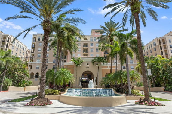 Front view of a multi-story building with a fountain and palm trees.