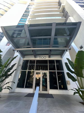 Front view of a high-rise building entrance with a glass canopy.