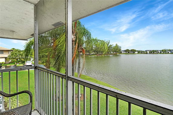 View from a balcony overlooking a lake with palm trees and distant residential buildings.