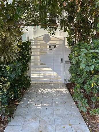 Front view of a house gate with a metal design surrounded by greenery.