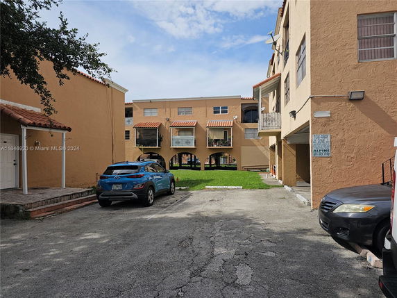 Outdoor parking area in front of a multi-story building with balconies.