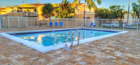 Outdoor swimming pool with surrounding fence and nearby buildings.