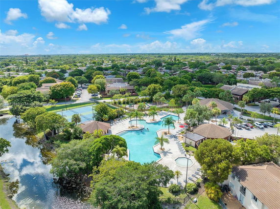 Aerial view of a community area featuring a swimming pool, tennis courts, and surrounding residential area.